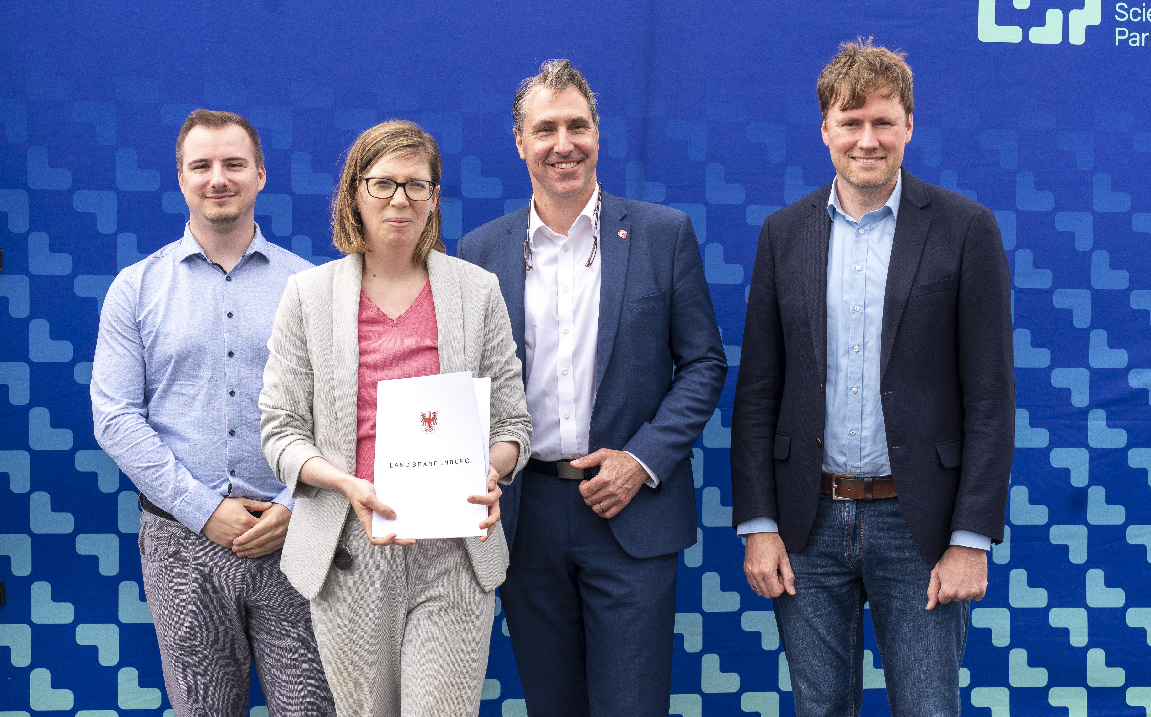 Marion Ernst hält Zuwendungsbescheid hoch, daneben stehen Matthias Schmid, Tim Berndt und Dr. Markus Schwenke